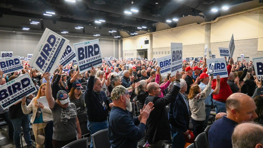 Image: A group of people in attendance at the Washington State Republican Party 2024 Convention hold up signs supporting Semi Bird as the gubernatorial candidate they wish to endorse.